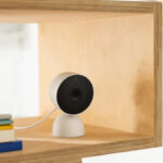 Google indoor wired home security camera placed on a bookshelf with books