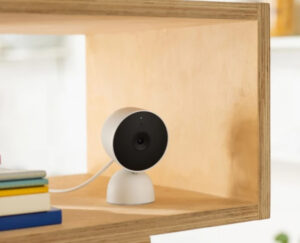 Google indoor wired home security camera placed on a bookshelf with books